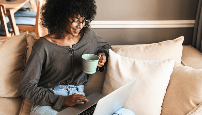 Woman sitting on couch drinking coffee and looking at laptop