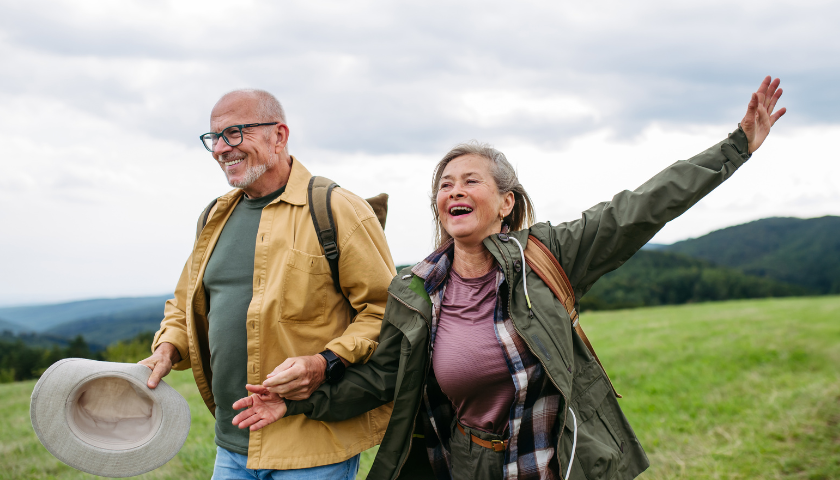 older couple holding hands walking on sandy beach next to ocean