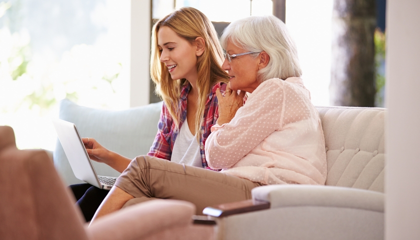 Younger woman and older woman sitting on couh looking at laptop together.