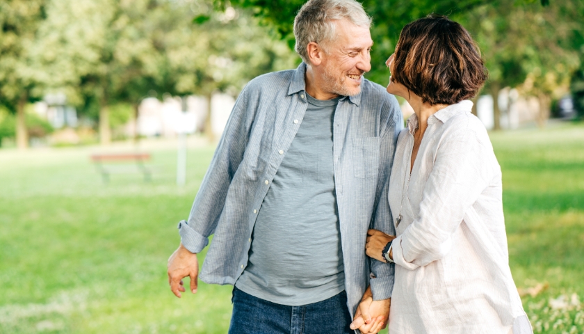 Elderly couple walking outside in park, holding hands.