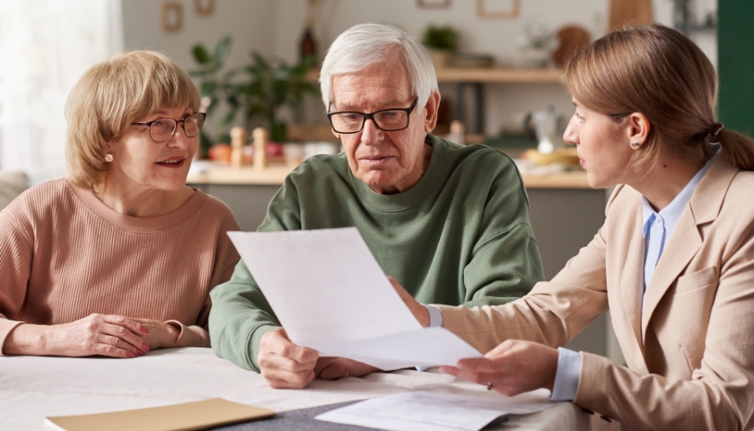 Older couple and young woman sitting around kitchen table looking at piece of paper together.